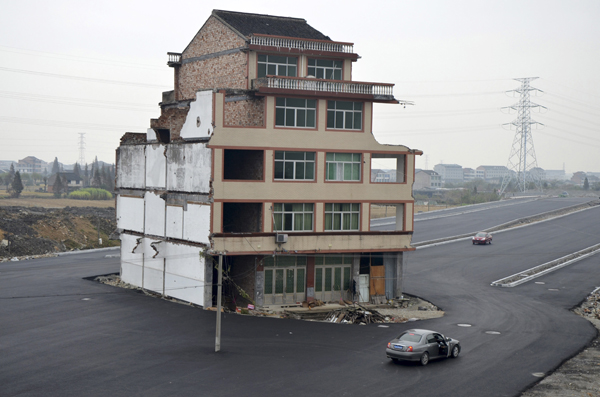 A car stops beside a house in the middle of a newly built road in Wenling, Zhejiang province, November 22, 2012. An elderly couple refused to sign an agreement to allow their house to be demolished. They say that compensation offered is not enough to cover rebuilding costs, according to local media. Their house is the only building left standing on a road which is paved through their village. REUTERS/China Daily